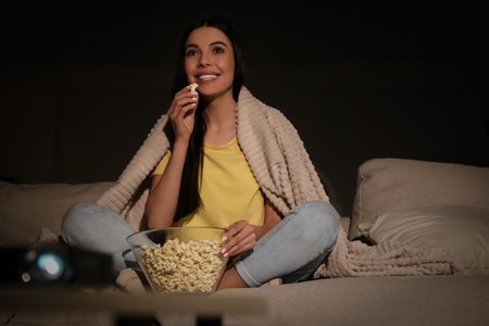 Young woman watching movie with popcorn on sofa at nightの写真素材