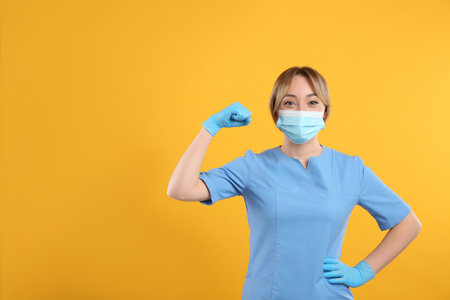 Doctor with protective mask showing muscles on yellow background, space for text. Strong immunity conceptの写真素材