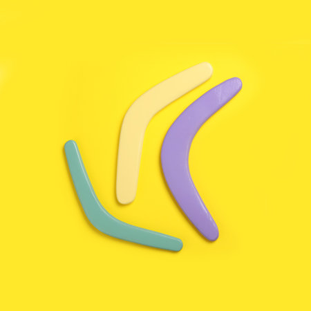 Colorful wooden boomerangs on yellow background, flat lay. Space for textの写真素材