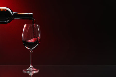 Pouring red wine from bottle into glass on dark background, space for textの写真素材