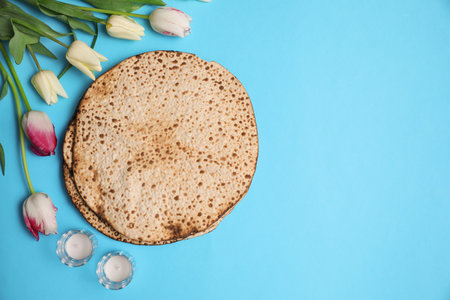 Tasty matzos, tulips and candles on light blue background, flat lay with space for text. Passover (Pesach) celebrationの写真素材