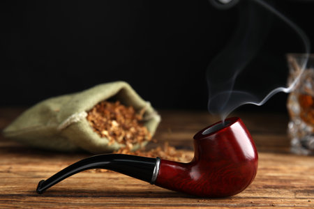 Stylish tobacco pipe with smoke on wooden tableの写真素材