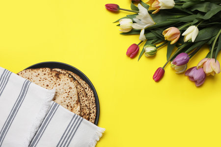 Tasty matzos and fresh flowers on yellow background, flat lay. Passover (Pesach) celebrationの写真素材