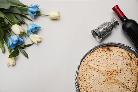 Tasty matzos, wine and tulips on light gray background, flat lay with space for text. Passover...