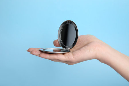 Woman holding stylish cosmetic pocket mirror on light blue background, closeupの写真素材
