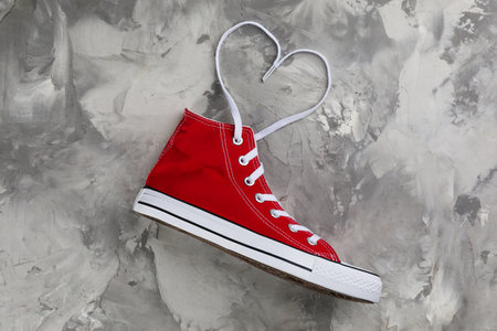 Red sneaker and white shoe lace in shape of heart on gray stone table, top viewの写真素材
