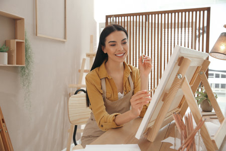 Young woman drawing on easel with pencil at table indoorsの写真素材