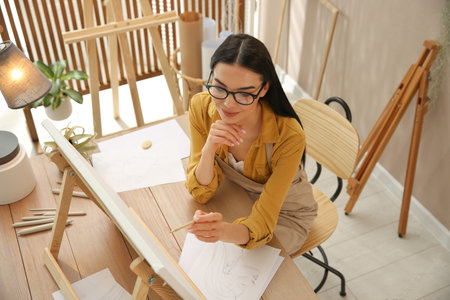 Young woman drawing on easel with pencil at table indoors, above viewの写真素材