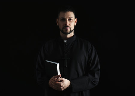 Priest in cassock with Bible on dark backgroundの写真素材