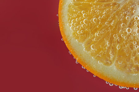 Fresh orange slice in sparkling water on red background, closeup. Space for textの写真素材