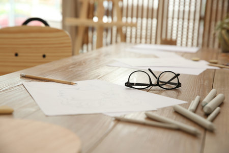 Male portrait drawing, pencils and glasses on wooden table in art studioの写真素材