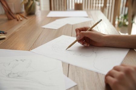 Young woman drawing male portrait at table indoors, closeupの写真素材