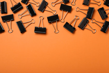 Black binder clips on orange background, flat lay. Space for textの写真素材