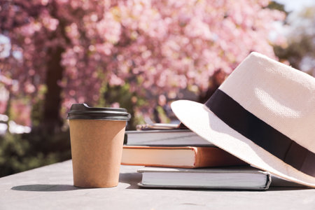 Stack of books, smartphone and hat on table in parkの写真素材