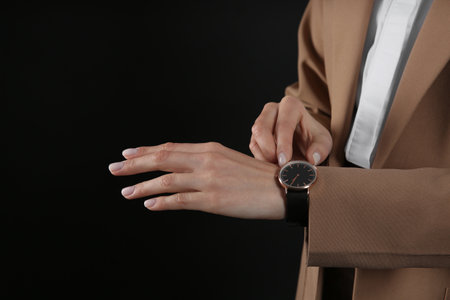 Businesswoman with wrist watch on black background, closeup. time managementの写真素材