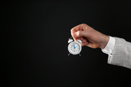 Closeup view of businessman holding tiny alarm clock on black background, space for text. time...