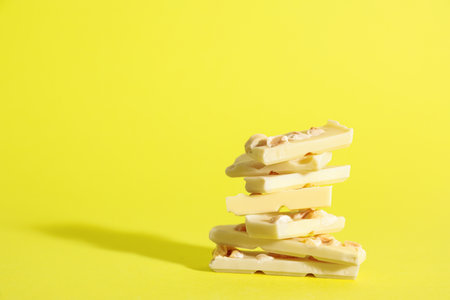 Stack of delicious white chocolate pieces with hazelnuts on yellow background, space for textの写真素材