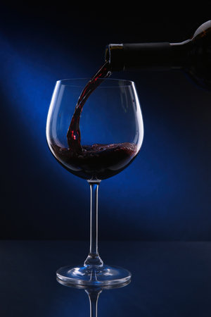 Pouring red wine from bottle into glass on color backgroundの写真素材