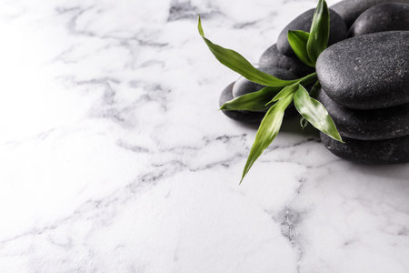 Spa stones and bamboo sprout on white marble table, space for textの写真素材