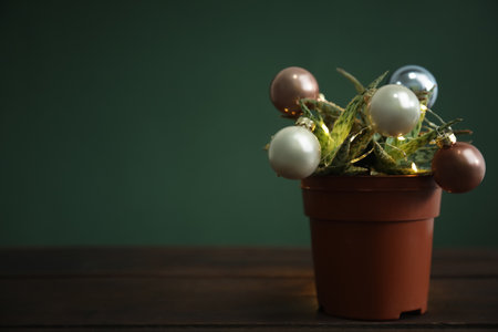Beautiful cactus with Christmas balls and festive lights on wooden table against green background,...