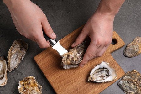 Man opening fresh oyster with knife at gray table, closeupの写真素材