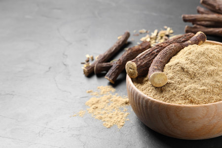 Powder in bowl and dried sticks of liquorice root on black table, space for textの写真素材
