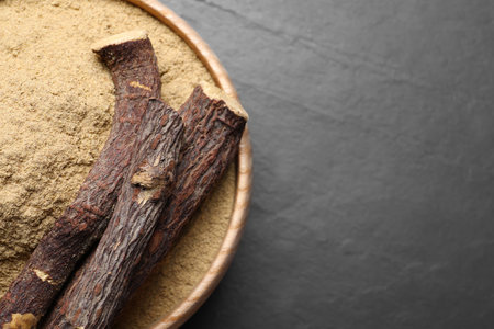 Powder in bowl and dried sticks of liquorice root on black table, top view. Space for textの写真素材