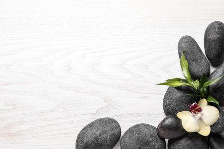 Spa stones, beautiful orchid flower and bamboo sprout on white wooden background, flat lay. Space for textの写真素材