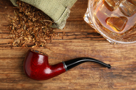 Smoking pipe with tobacco and glass of whiskey on wooden table, flat layの写真素材