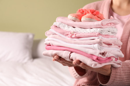 Woman holding stack of baby girl's clothes with shoes indoors, closeup. Space for textの写真素材