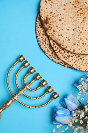 Tasty matzos, flowers and menorah on light blue background, flat lay. Passover (Pesach) celebrationの写真素材