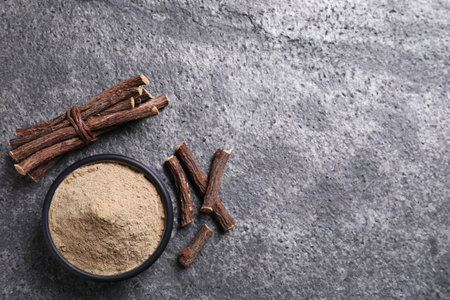 Powder in bowl and dried sticks of liquorice root on gray table, flat lay. Space for textの写真素材
