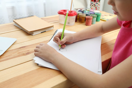 Little girl drawing on paper with pencil at online lesson indoors, closeup. distance learningの写真素材