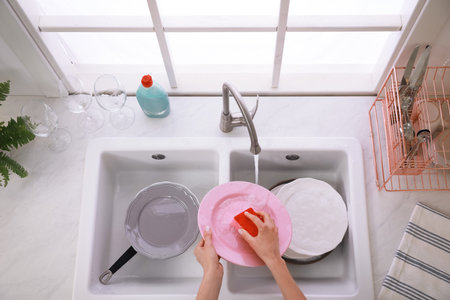Woman washing plate above sink in kitchen, closeupの写真素材