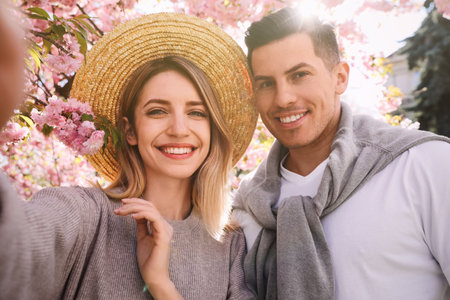 Happy couple taking selfie near blossoming sakura outdoors on spring dayの写真素材