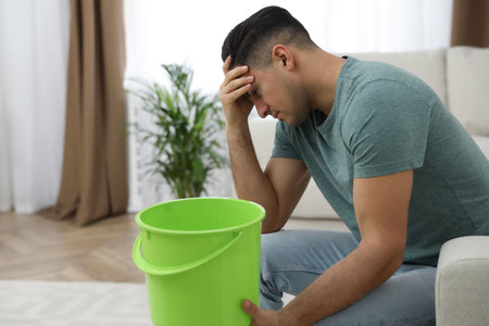 Emotional man collecting water leaking from ceiling in living room. Damaged roofの写真素材