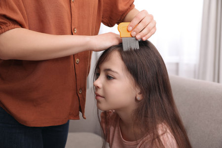 Mother using nit comb on her daughter's hair indoors. Anti-lice treatment