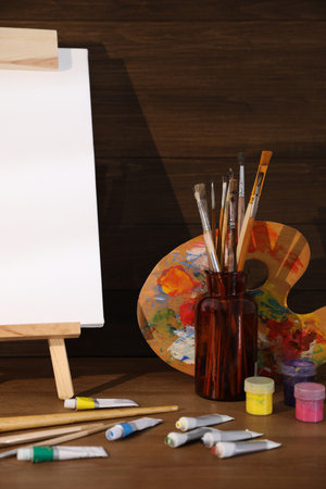 Easel with canvas and art supplies on wooden tableの写真素材
