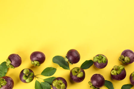 Fresh ripe mangosteen fruits with green leaves on yellow background, flat lay. Space for textの写真素材