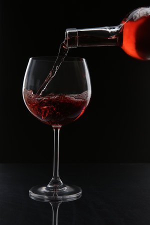 Pouring red wine from bottle into glass on black backgroundの写真素材