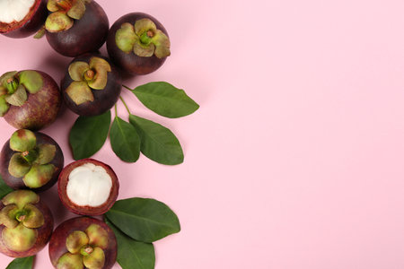Fresh ripe mangosteen fruits with green leaves on pink background, flat lay. Space for textの写真素材
