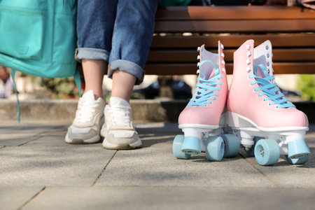 Woman with stylish pink roller skates sitting on bench outdoors, closeupの写真素材