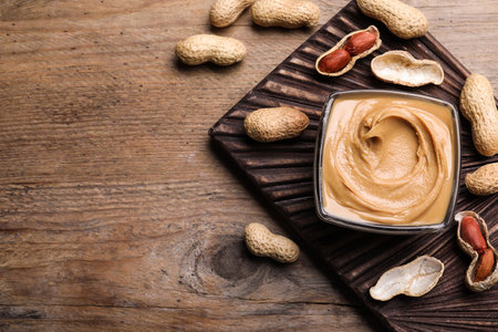 Yummy peanut butter in glass bowl on wooden table, flat lay. Space for textの写真素材