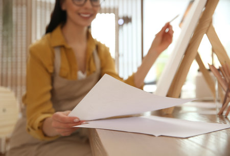 Young woman taking sheet of paper for drawing at table indoors, closeupの写真素材