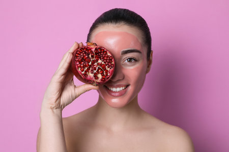 Woman with pomegranate face mask and fresh fruit on pink backgroundの写真素材