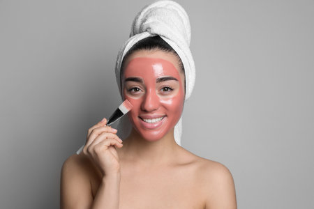 Woman applying pomegranate face mask on grey backgroundの写真素材