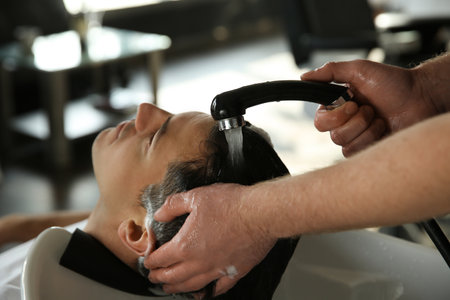 Professional barber washing client's hair at sink in salon, closeupの写真素材