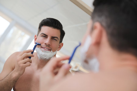 Handsome man shaving near mirror in bathroomの写真素材