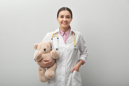 Pediatrician with teddy bear and stethoscope on light grey backgroundの写真素材