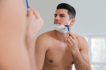 Handsome man shaving near mirror in bathroomの写真素材